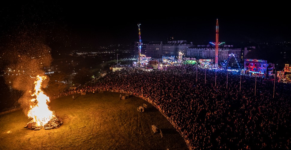 Crowds looking at the bonfire on Plymouth Hoe, with the fairground in the background